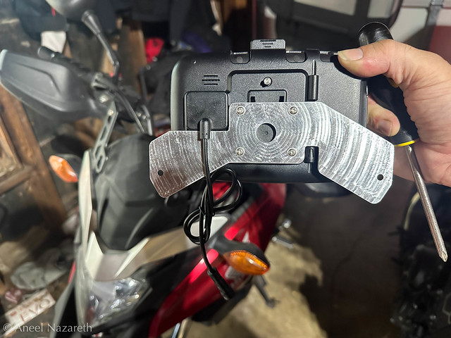 A complicated flat shape is screwed on to the back of a device. There are multiple cutouts to accommodate various things hanging off of the device