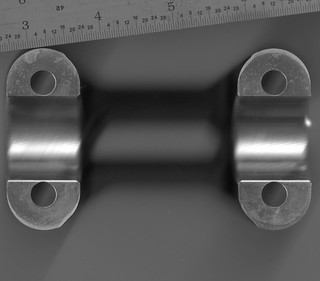 A scan of the bottom of the bracket. The four bolt holes are visible, along with the semi-circle that holds the bar tubing. There is a ruler in the scan, marked in inches for some strange reason