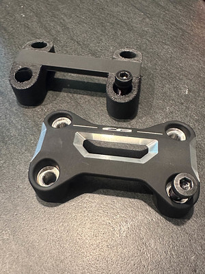 A simplified version of the factory clamp next to the factory clamp. The simplified version is basically four bolt holes and a spacer bar.