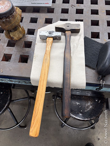 Two completed hammers. One has two square ends and a light wood handle. The other has one square end and one tapered end and a dark wood handle