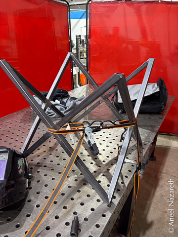 An orange ratchet strap is wrapped around the tubes of the table to get the last couple corners to meet up nicely.