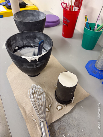 A cylindrical metal flask filled to the brim with plaster sits next to a whisk and a bowl of investment