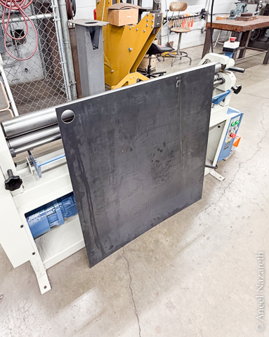 The sheet metal panel with doorknob hole leans against the roller machine